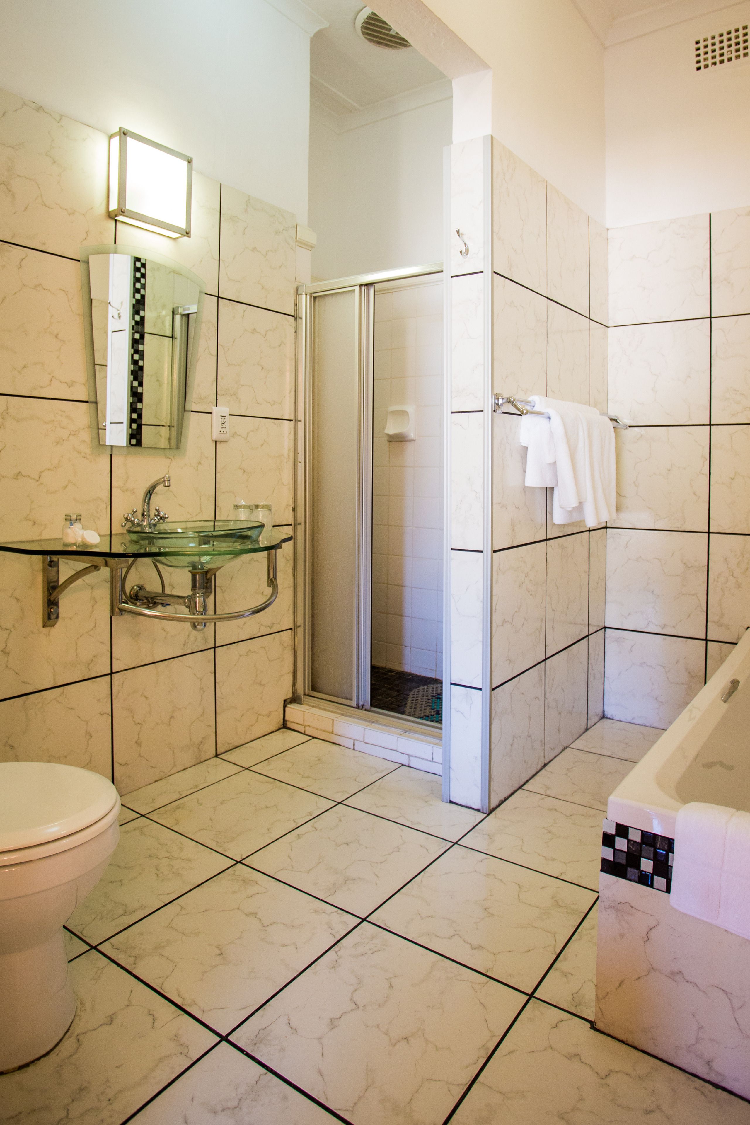 A bathroom with a glass sink, a toilet, a shower, and a bathtub.