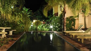 Un espace piscine nocturne doté d’une piscine à eau claire, de chaises longues et d’une végétation luxuriante.