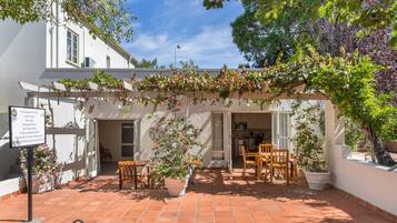 Une cour avec une pergola recouverte de plantes, des sièges d’extérieur et un panneau indicateur.