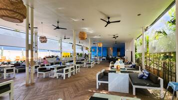 A spacious restaurant with high ceilings, multiple ceiling fans, and a mix of seating arrangements including tables and sofas.