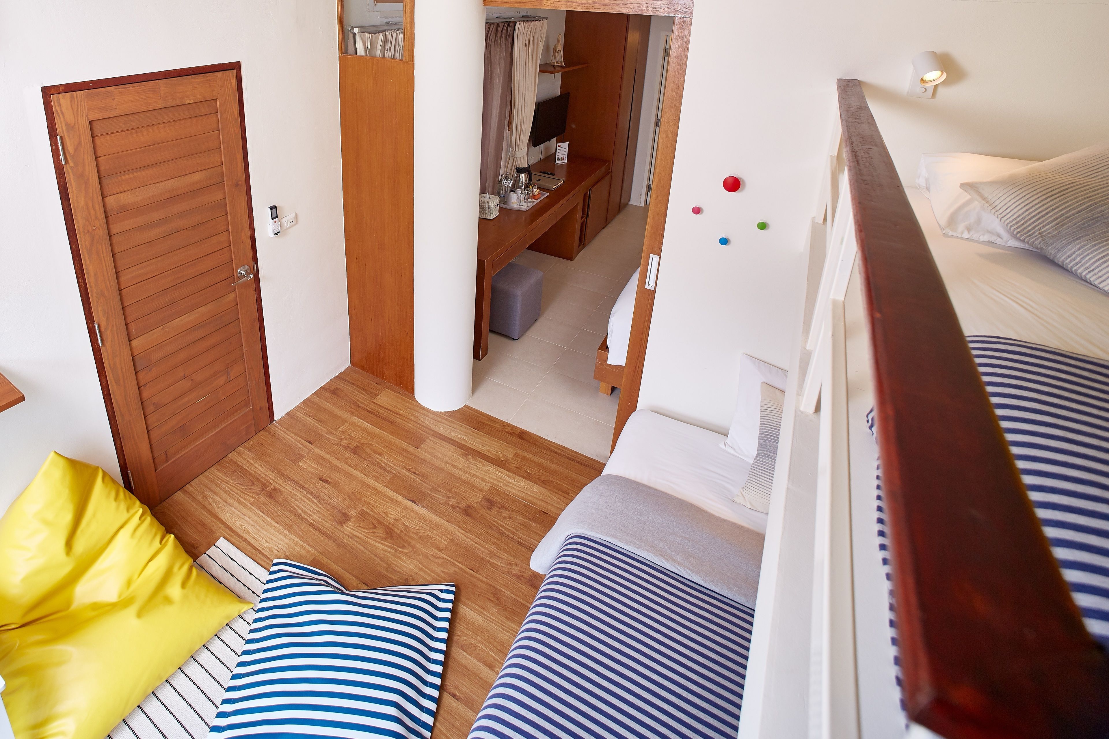 Een slaapkamer met een houten vloer, een bed met gestreept beddengoed, een geel kussen en een houten garderobe.