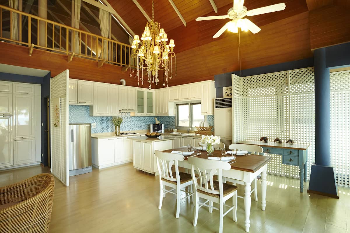 A spacious kitchen with white cabinetry, a central island, and a dining area with white chairs.
