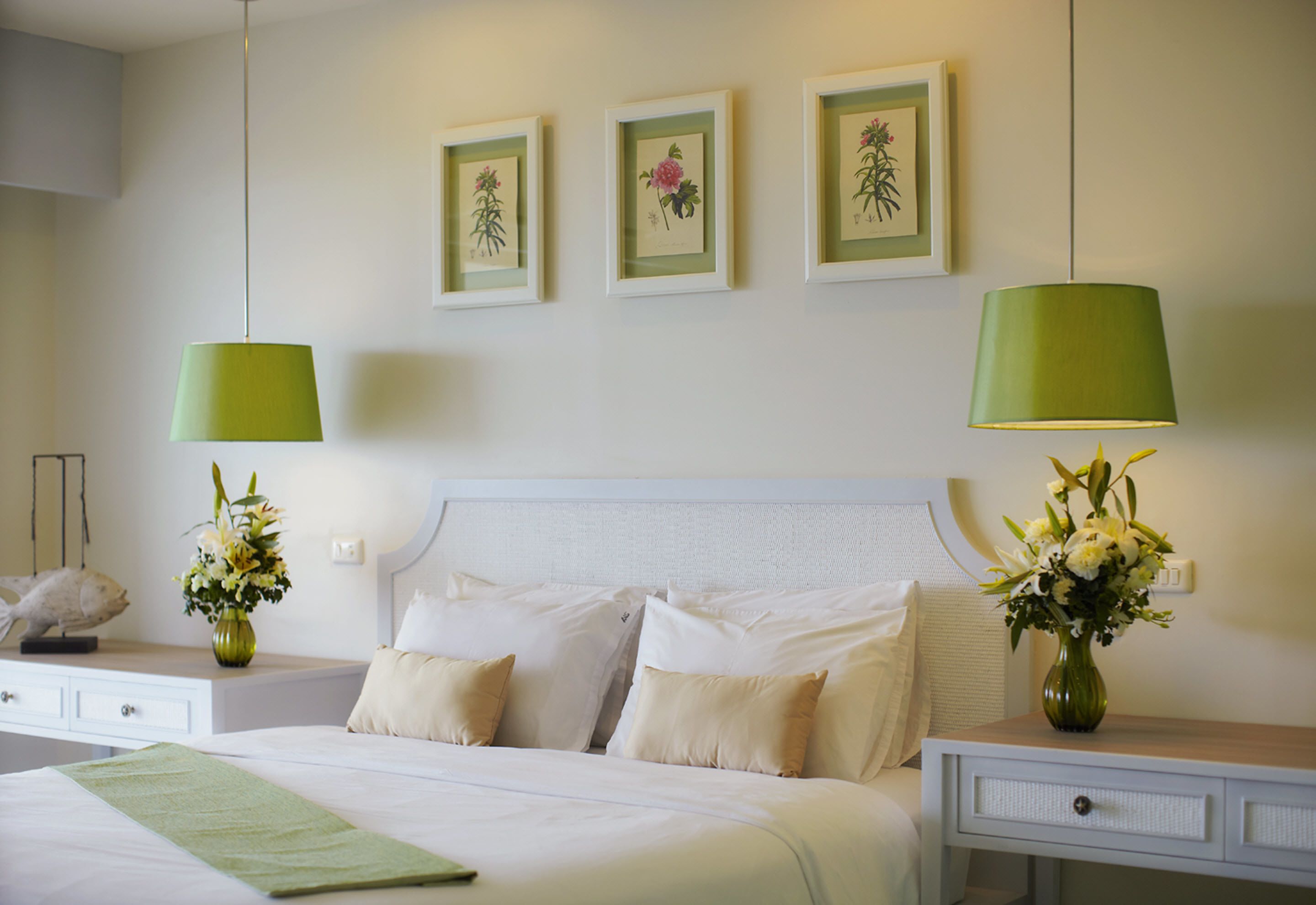 Habitación de hotel con una cama, dos mesitas de noche, un aparador y tres láminas botánicas enmarcadas en la pared.