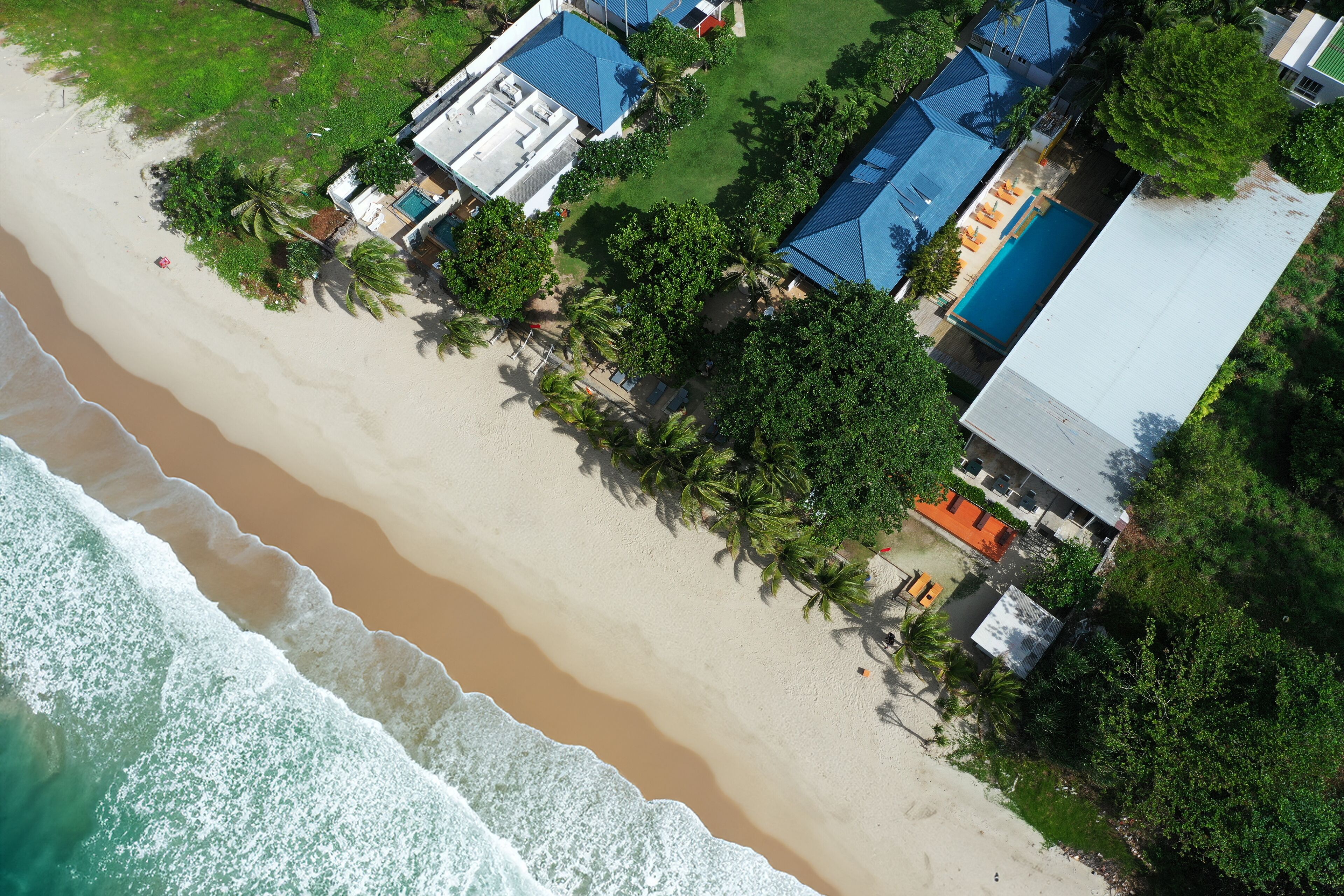 An aerial view of a beachside property with multiple buildings, a swimming pool, and a beachfront.