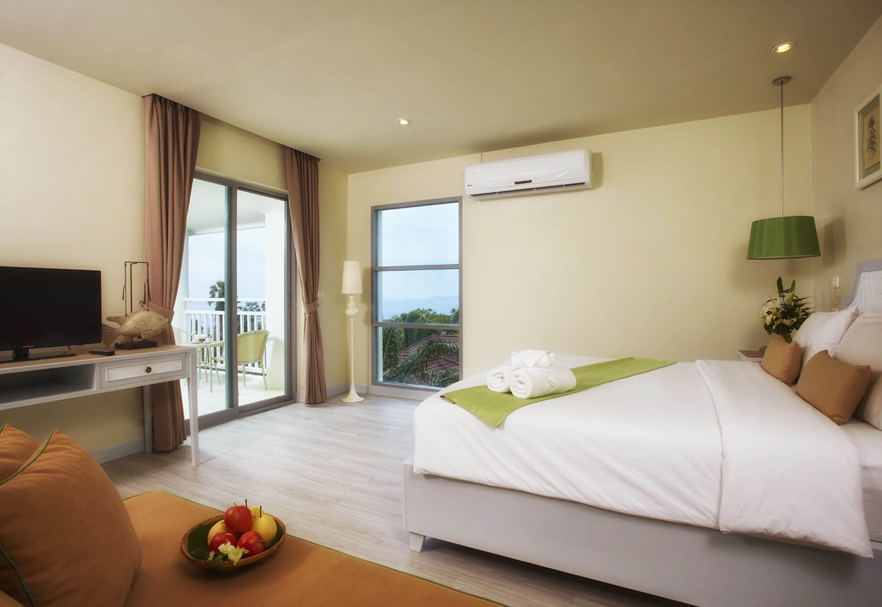 Een hotelkamer met een bed, een bureau met een televisie, een balkon en uitzicht op de omgeving.