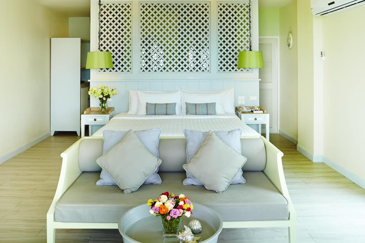 A modern bedroom with a bed, two nightstands, a sofa, and a decorative vase with flowers.
