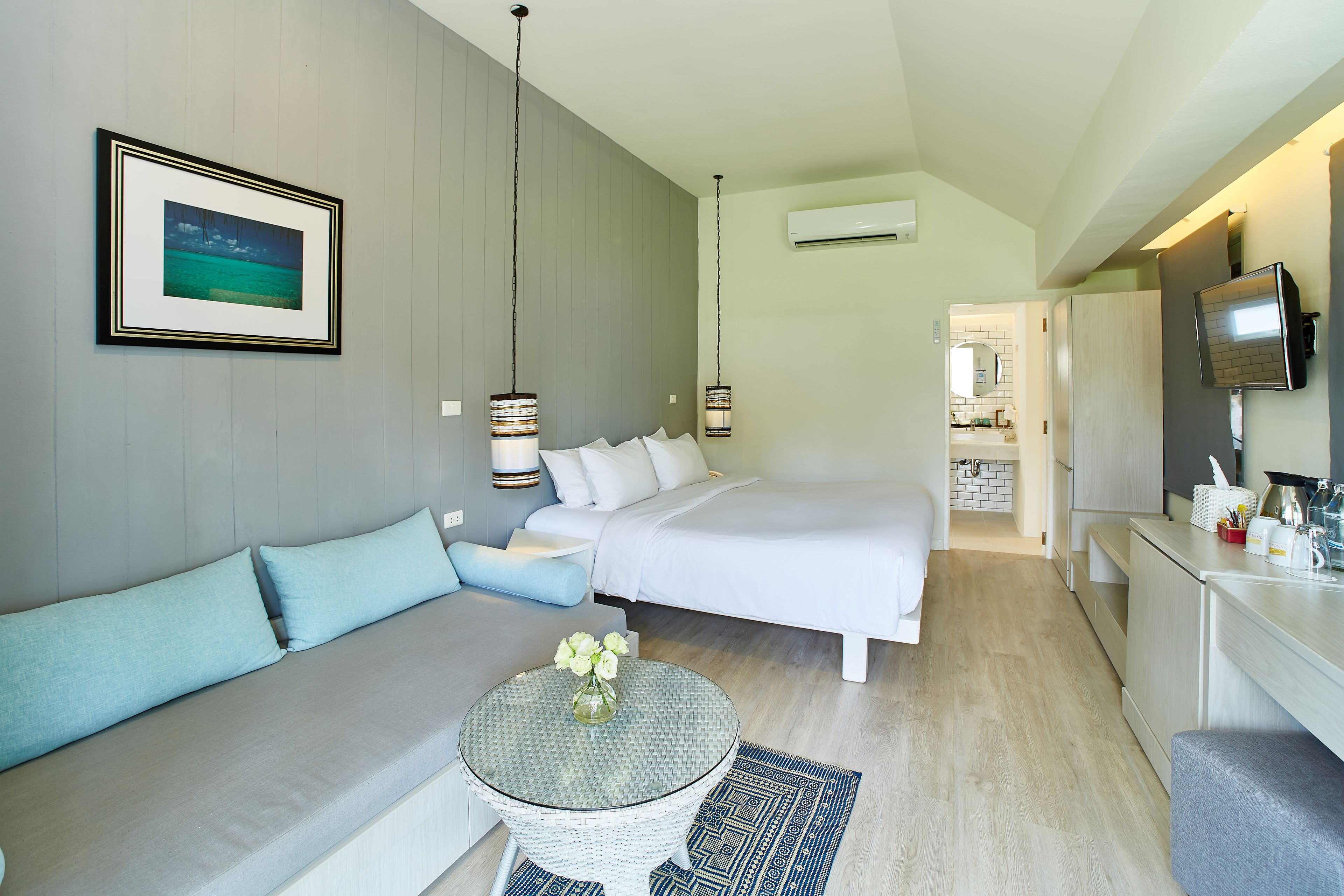 A modern hotel room with a bed, sofa, dining area, and kitchen.