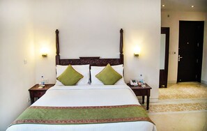 A hotel room with a large bed, two bedside tables, and a door leading to another room. - Mantra Amaltas (New Delhi)