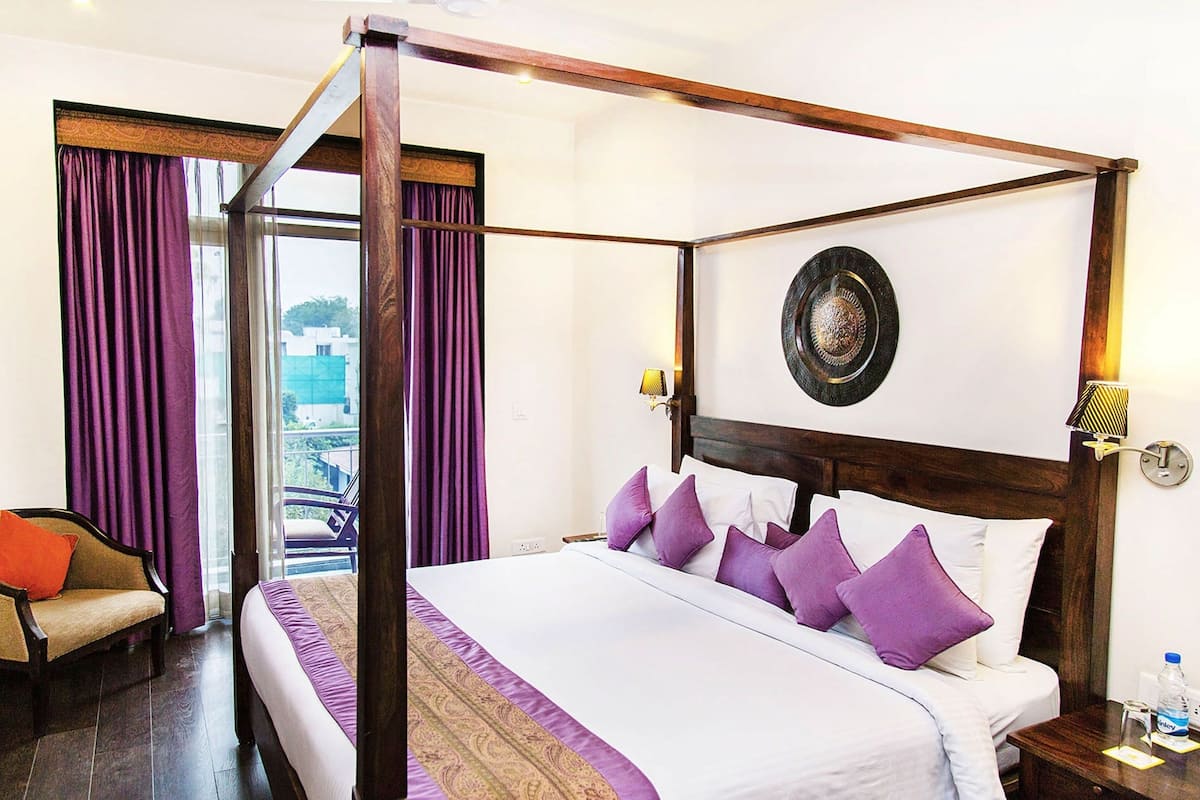 A four-poster bed with a headboard, a chair, a nightstand, and a view of the outdoors.