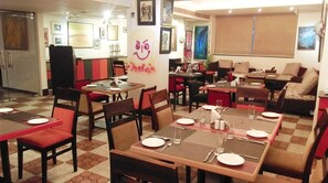 Ein Restaurant mit mehreren Tischen und Stühlen, einige mit roten Kissen. An den Wänden befinden sich gerahmte Kunstwerke.