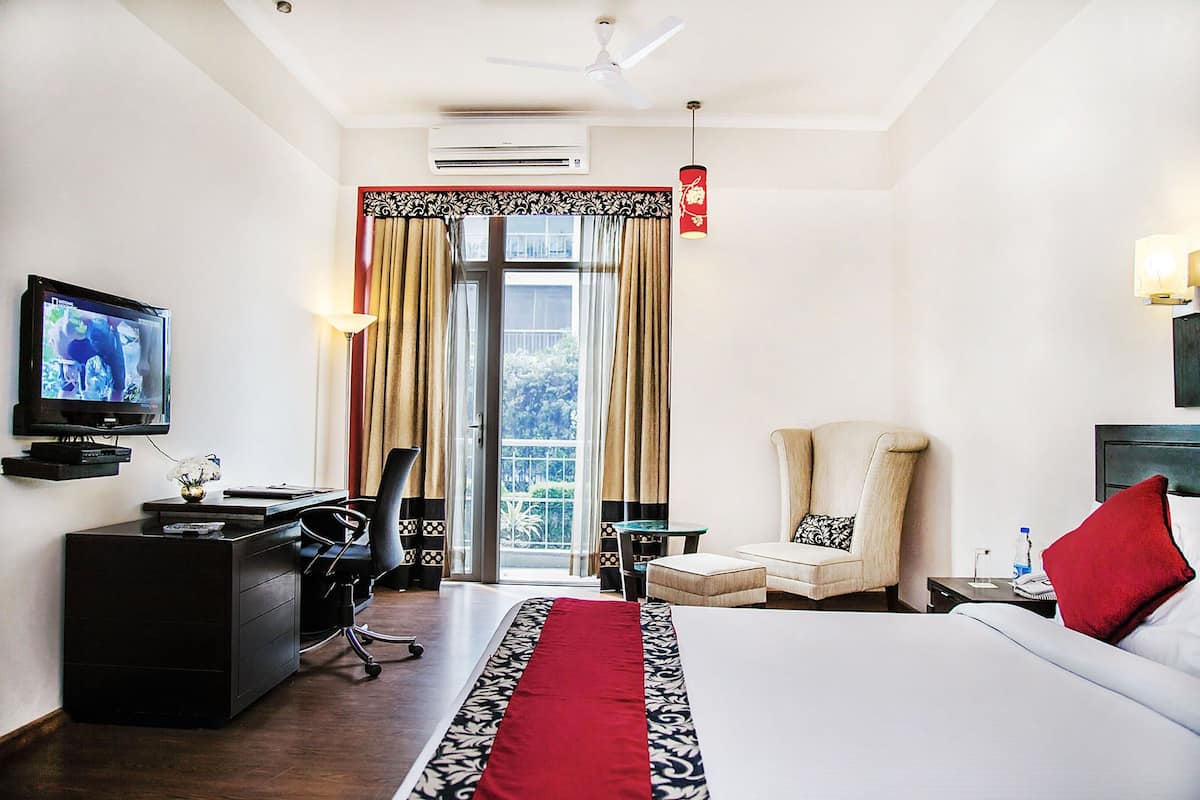 A hotel room with a bed, desk, chair, television, and a view of the outdoors.