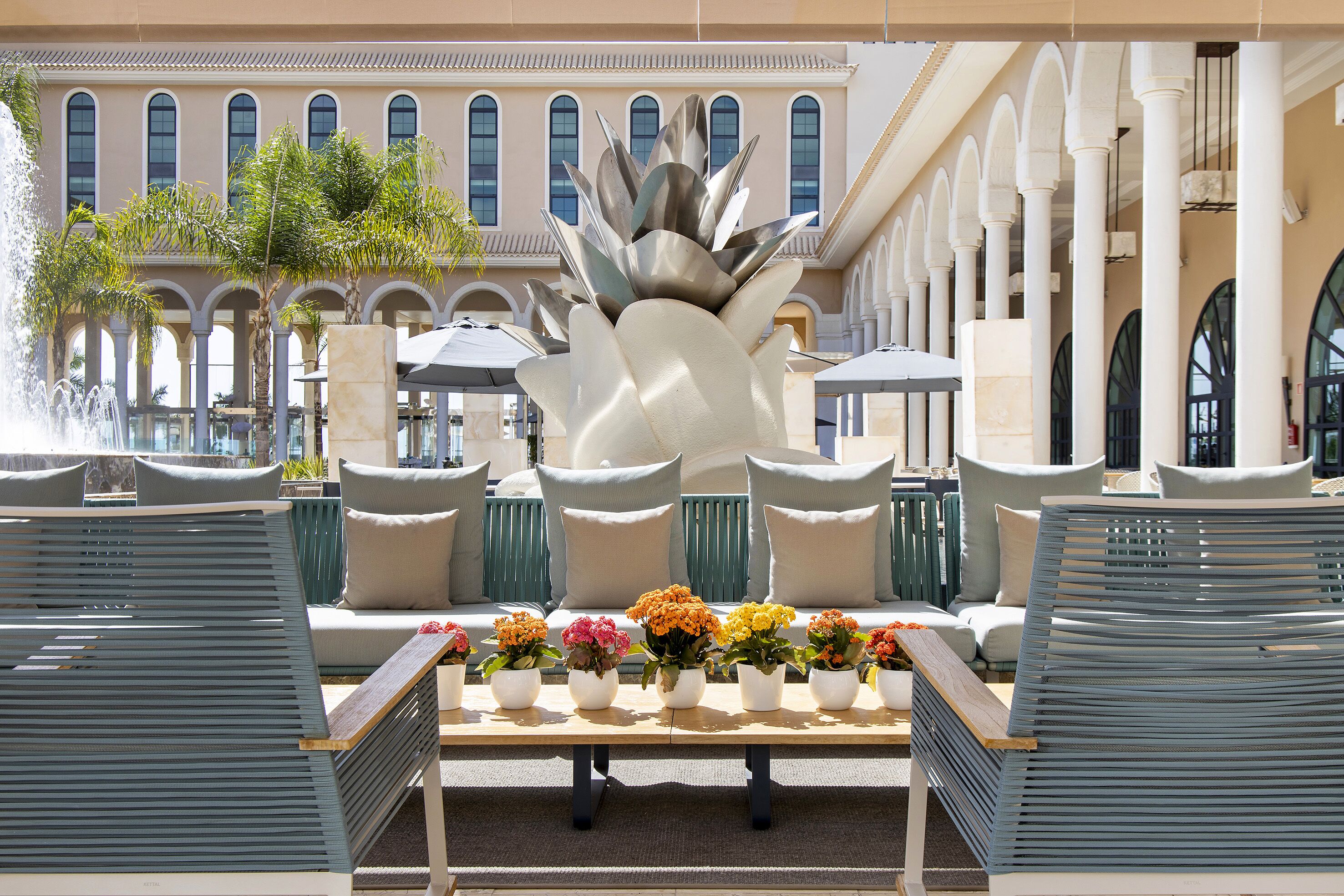 Zona junto a la piscina con una fuente, una fila de sillas y una mesa decorada con arreglos florales.