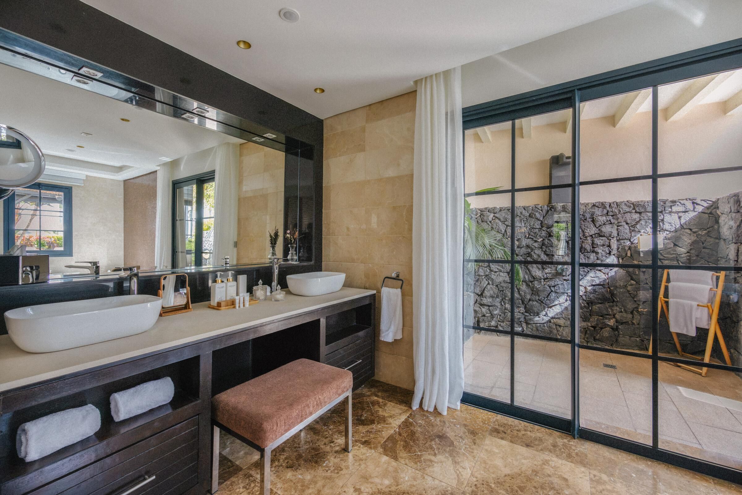 Une salle de bain moderne avec deux lavabos, un grand miroir et un banc.