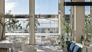 A spacious dining area with high ceilings, large windows, and a view of palm trees and the ocean. - RedLevel at Gran Melia Palacio de Isora - Adults Only (Guia de Isora)