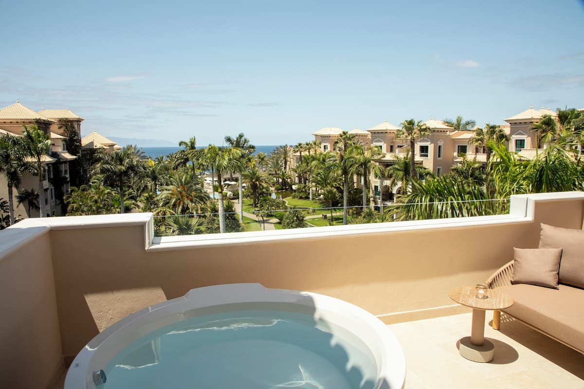 Ein Balkon mit Whirlpool, einer Couch und Blick auf einen Kurort mit Palmen und Gebäuden.