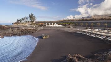 On the beach, black sand, sun-loungers, beach umbrellas