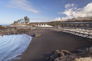On the beach, black sand, sun loungers, beach umbrellas