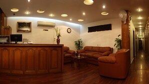 A reception area with a wooden desk, brown leather sofas, a clock, and a wall-mounted air conditioner.