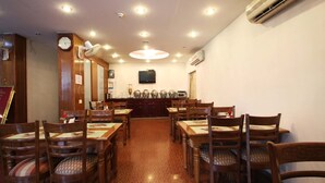 A restaurant with wooden tables and chairs, a clock on the wall, and an air conditioning unit.