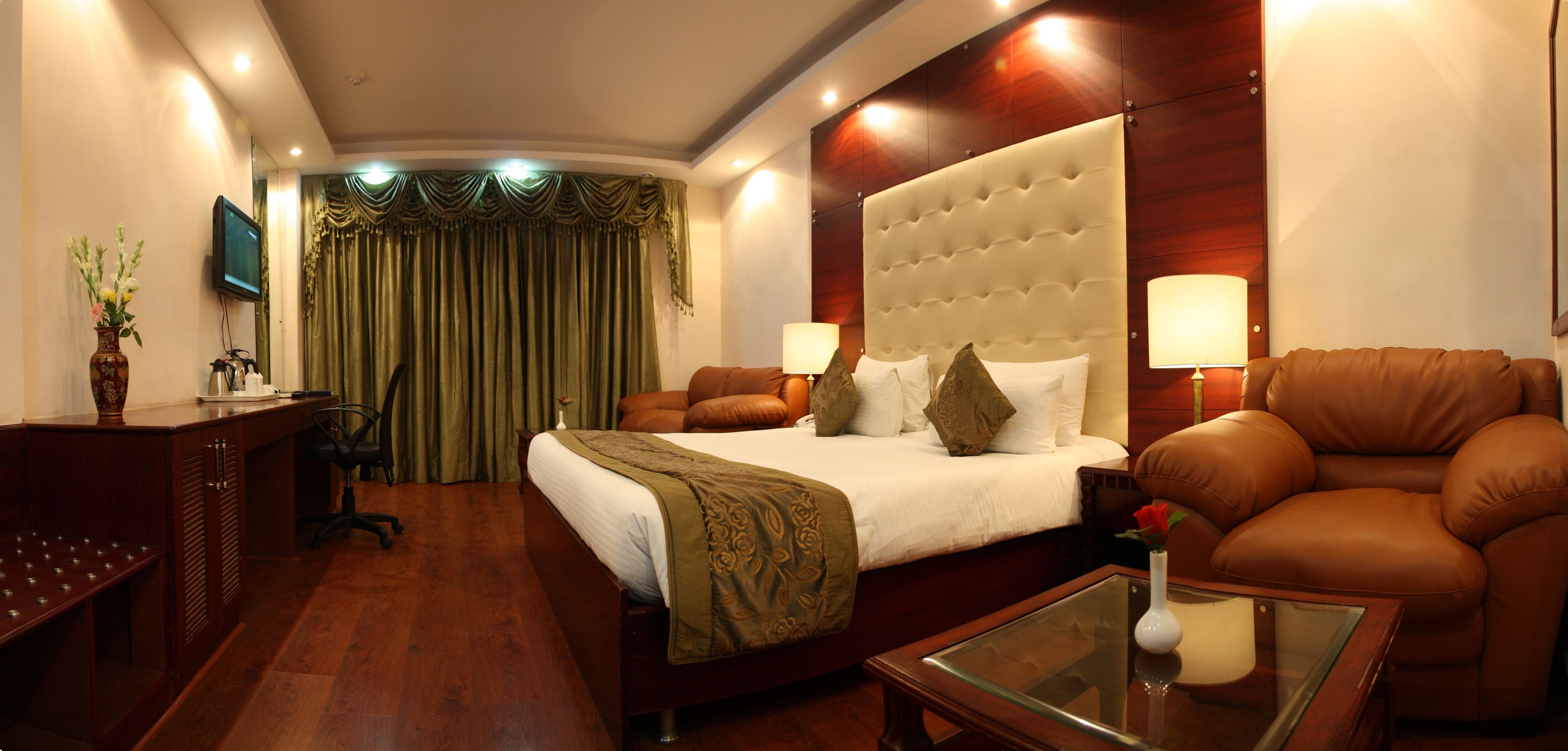 A hotel room with a large bed, two bedside tables, a desk with a chair, a sofa, and a TV.