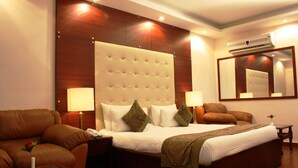 A hotel room with a large bed, two bedside tables, a nightstand, a sofa, a glass coffee table, and a mirror on the wall.