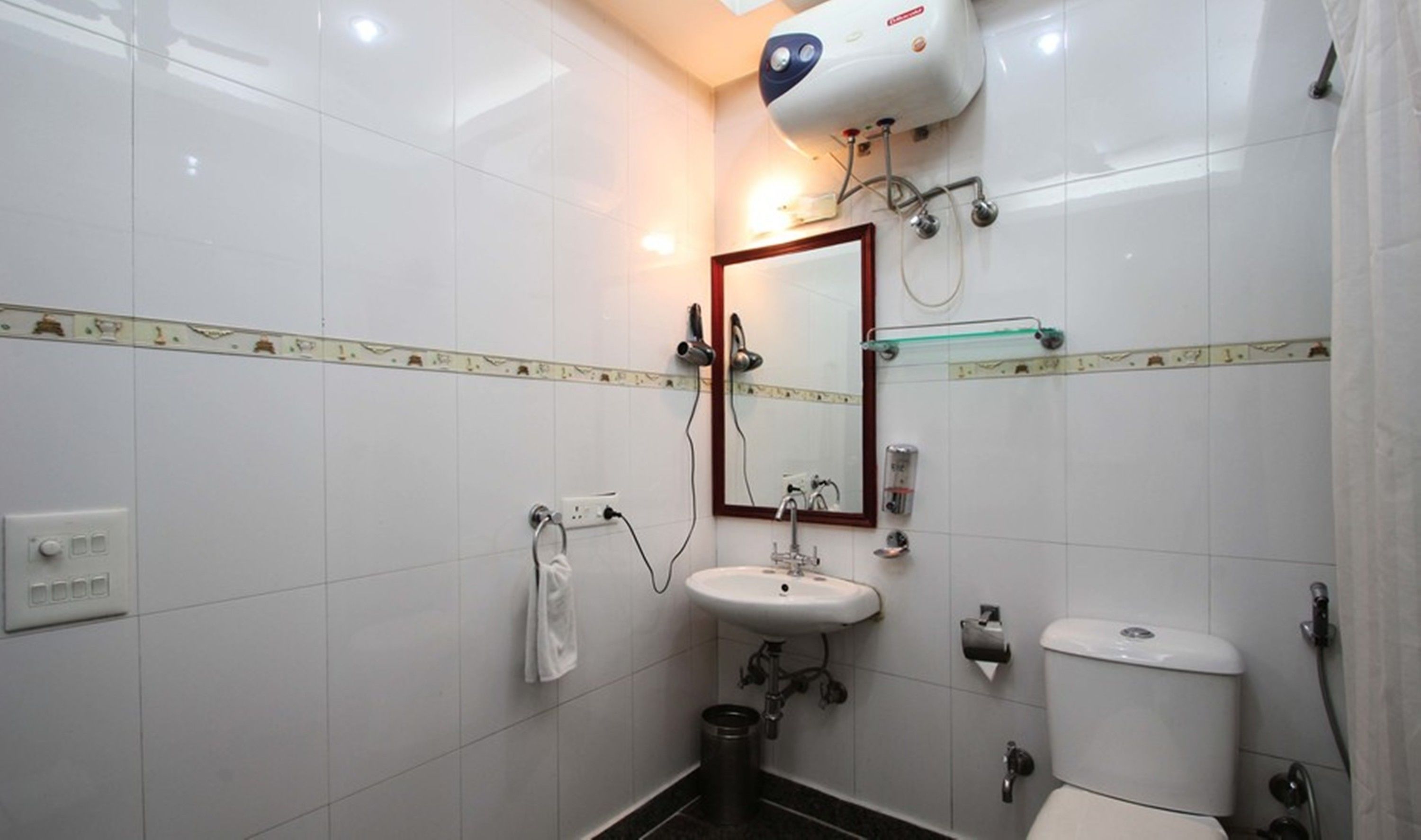 A bathroom with white tiles, a sink, a toilet, a mirror, and a hairdryer.