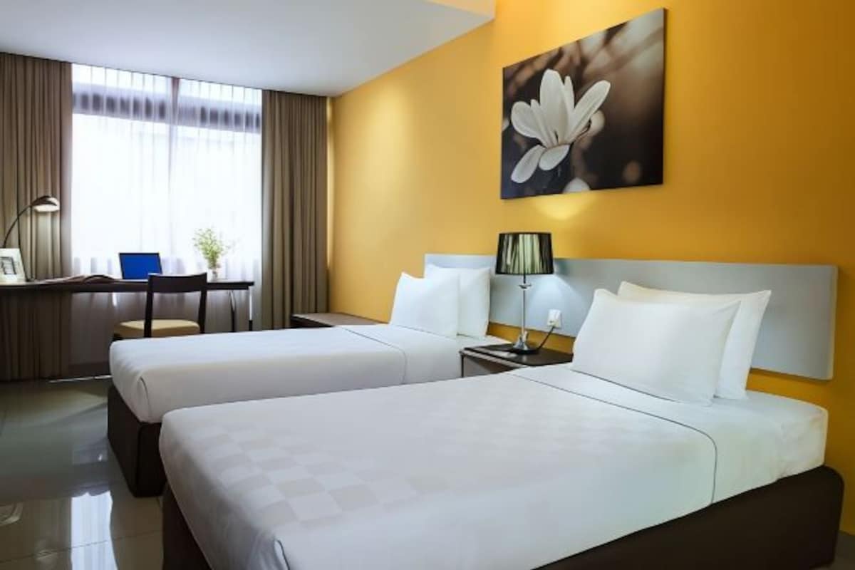 A hotel room with two beds, a desk, a chair, and a lamp.