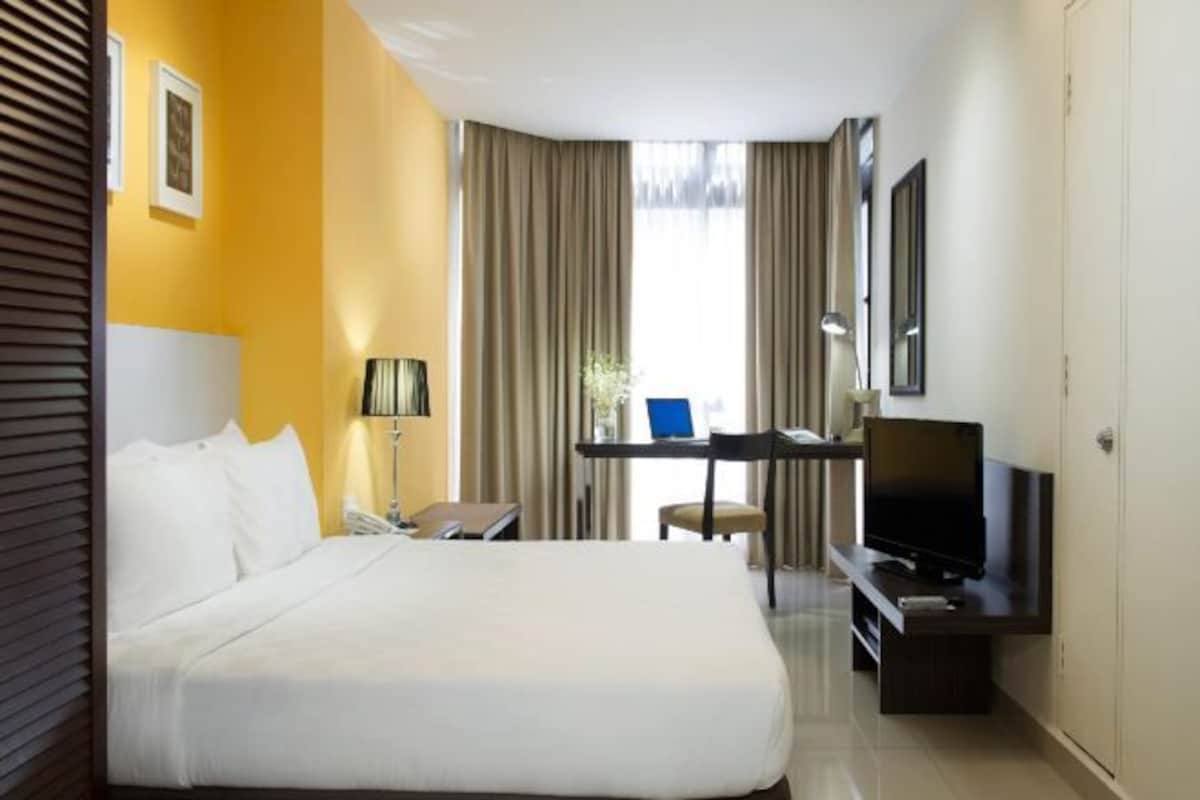 A hotel room with a bed, desk, TV, and curtains.