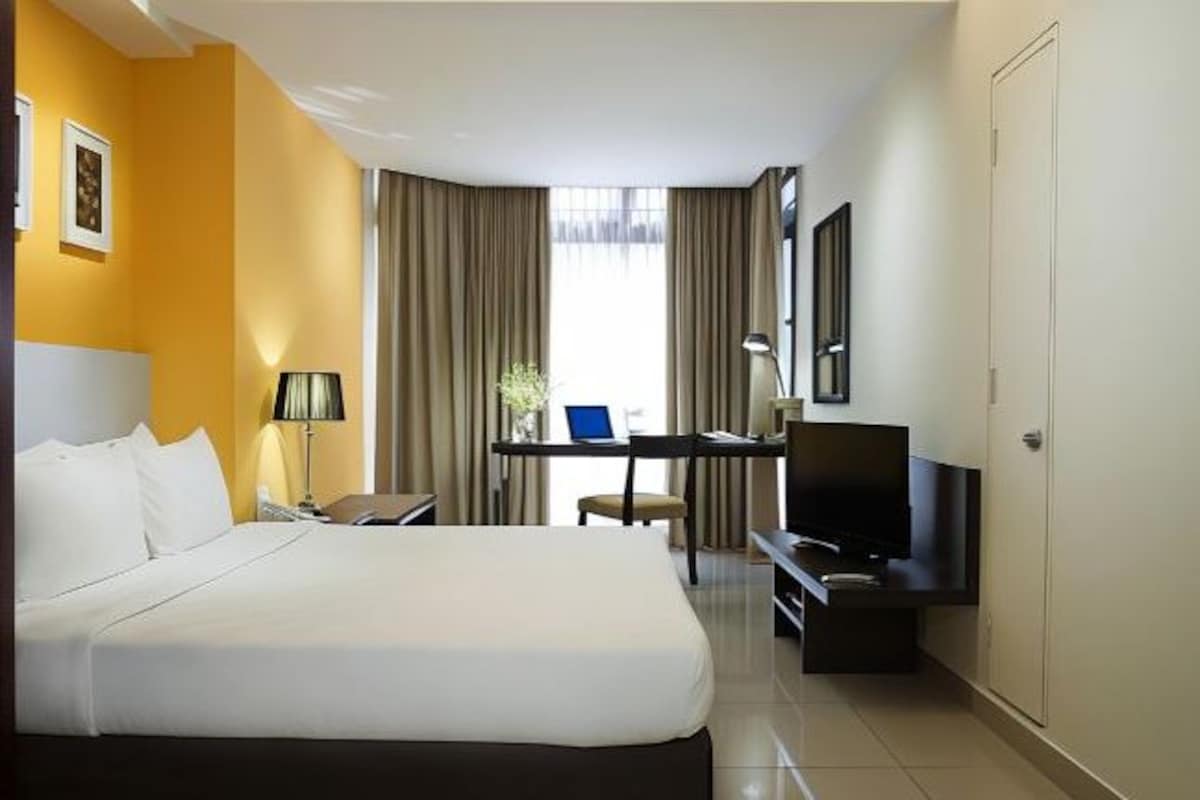 A hotel room with a large bed, a desk with a computer, a TV, and a chair.