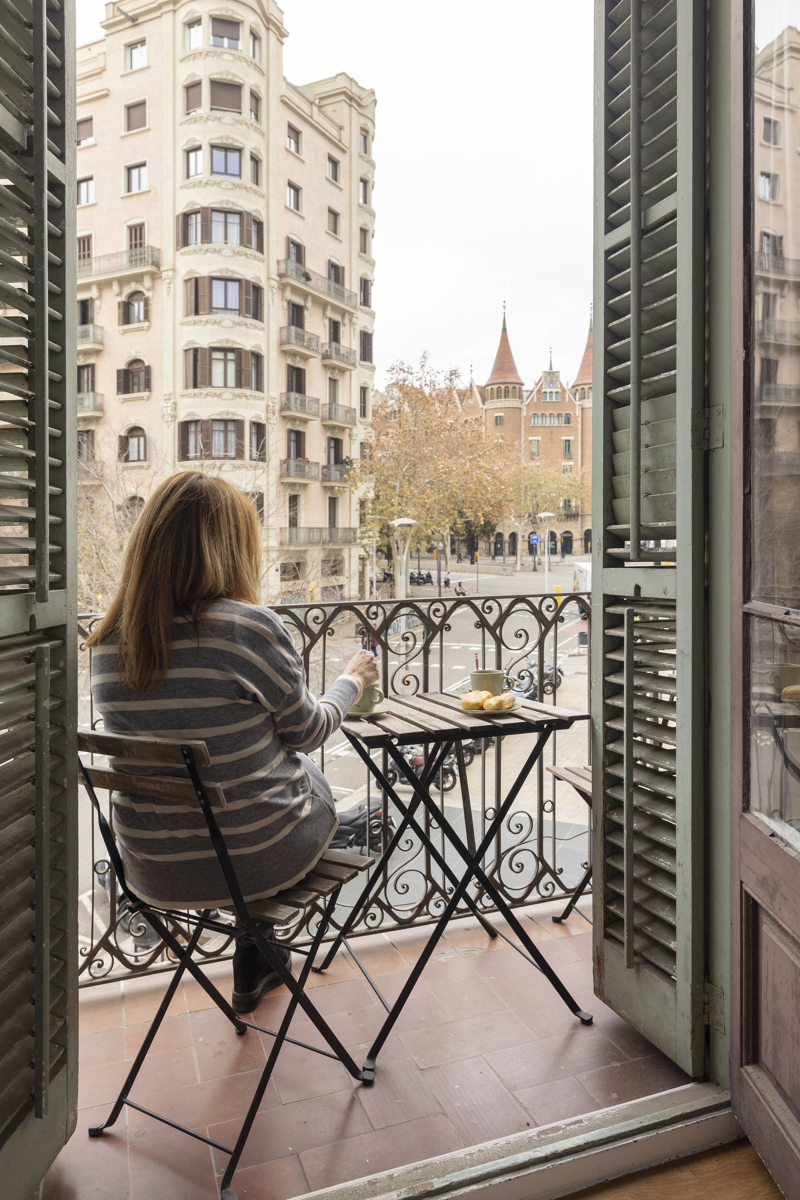 Una persona sentada a una mesa en un balcón con vistas a edificios y árboles.