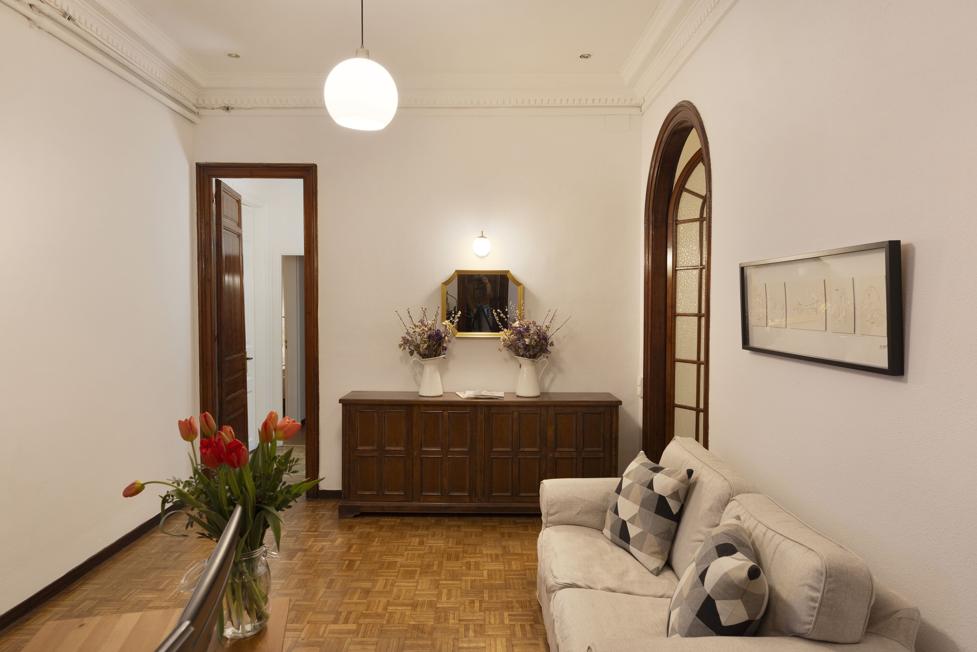 Un pasillo con suelo de madera, pared blanca, un mueble de madera con espejo y un cuadro enmarcado.