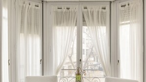 Une pièce avec deux fauteuils blancs, une petite table ronde et de fines rideaux blancs.