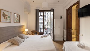 Une chambre d’hôtel avec un grand lit, un plus petit lit, une télévision, une armoire, une salle de bain et un balcon donnant sur des immeubles.