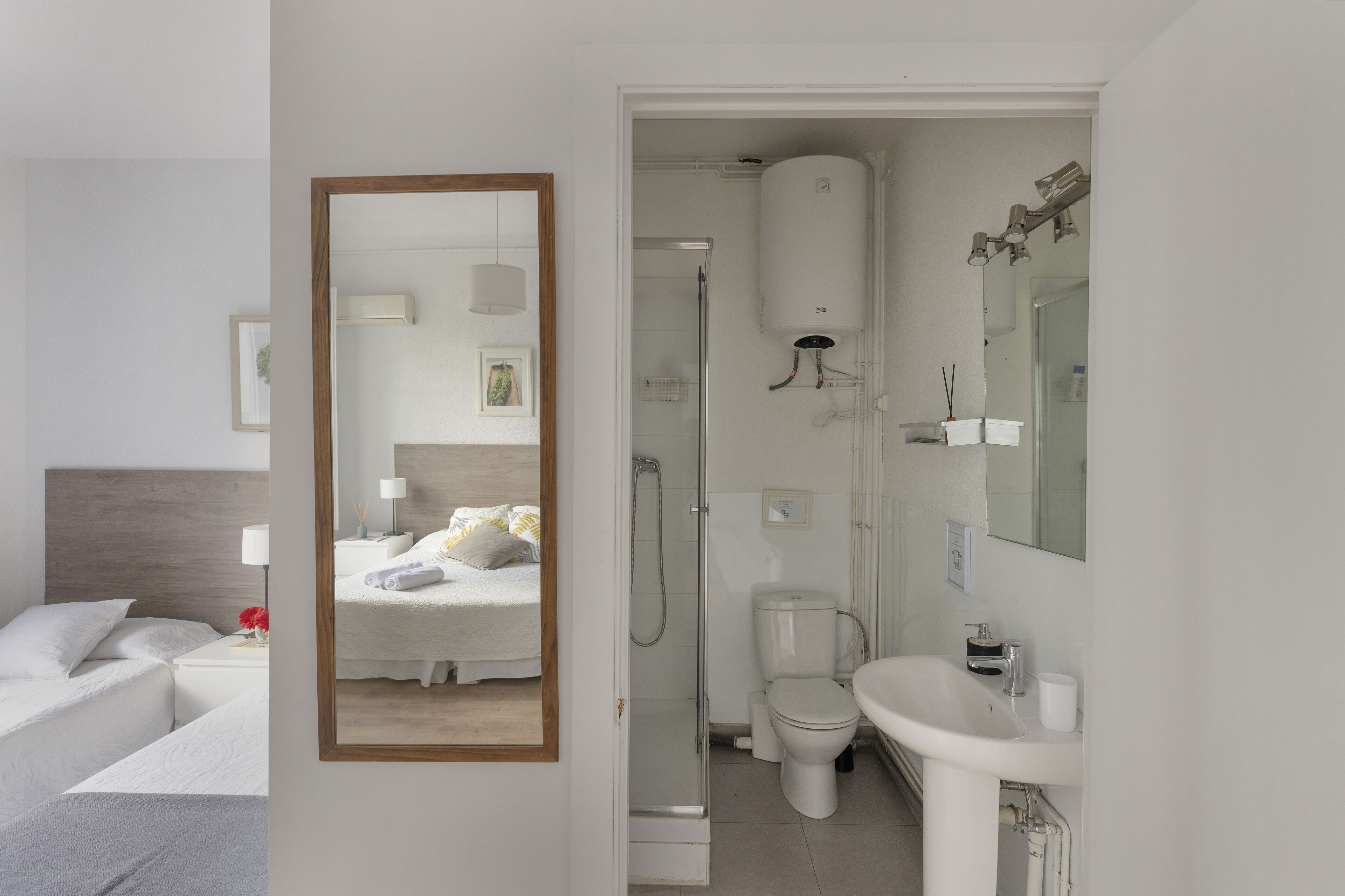 A hotel room with a bed, bedside table, and a large mirror.