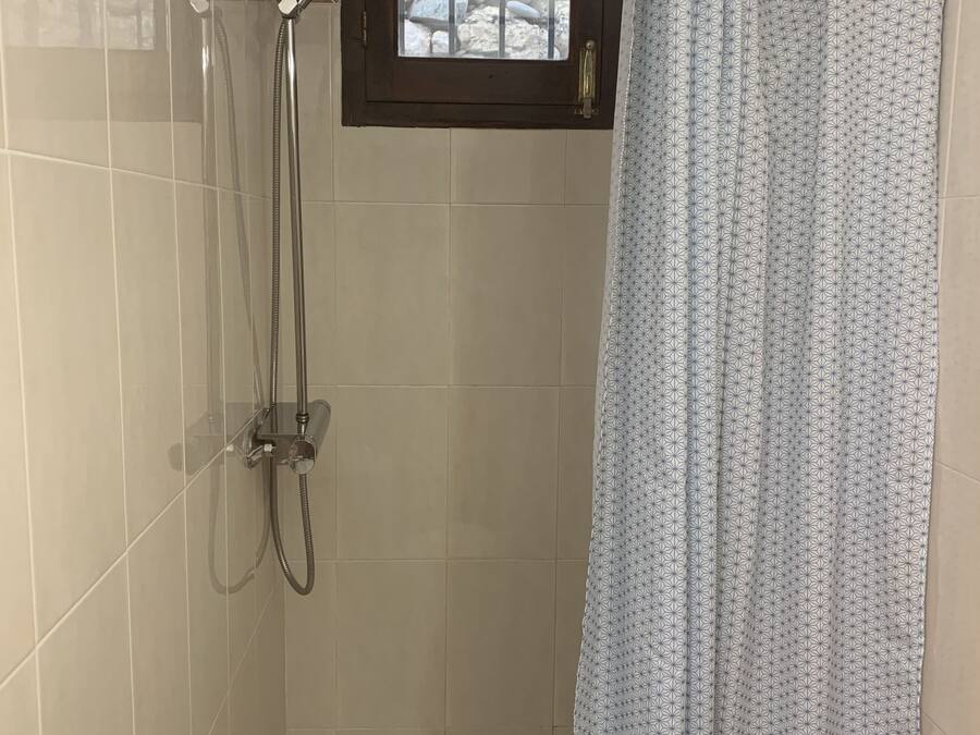 Un espace douche doté d’une porte en verre, d’une fenêtre située au-dessus de la douche et d’un rideau.