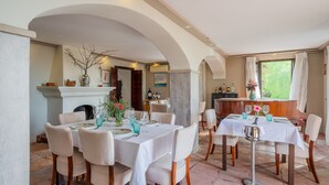 A dining area with round tables, chairs, and a fireplace. There is a bar area with bottles and a vase of flowers. - LA TARTANA HOTEL BOUTIQUE (Almunecar)