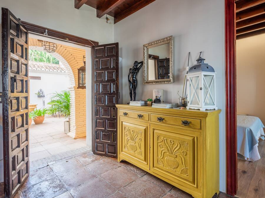 A room with a wooden door, a yellow cabinet with floral carvings, a mirror, and a white lantern.