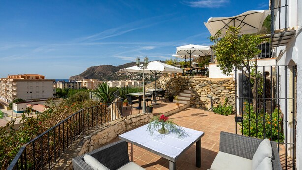 An outdoor patio with wicker furniture, a table with a vase of flowers, and umbrellas. - LA TARTANA HOTEL BOUTIQUE (Almunecar)