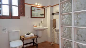 A bathroom with a toilet, sink, and a mirror. There is a sign on the wall and a towel rack with towels.