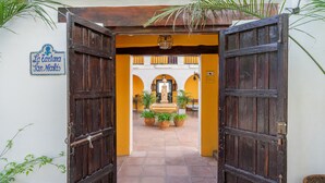 An open wooden gate leading to a courtyard with potted plants and a sign reading "La Cortana San Miguel". - LA TARTANA HOTEL BOUTIQUE (Almunecar)