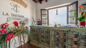 A rustic interior with a sign reading "LA TARTANA LA HERRADURA," a wooden cabinet, a window with a view, and a potted plant. - LA TARTANA HOTEL BOUTIQUE (Almunecar)