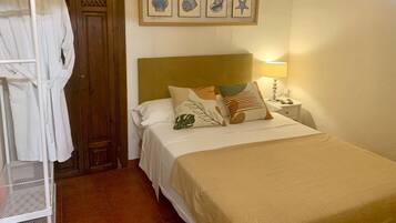 A bedroom with a bed, a nightstand, a lamp, a wall-mounted air conditioner, and a wooden door.