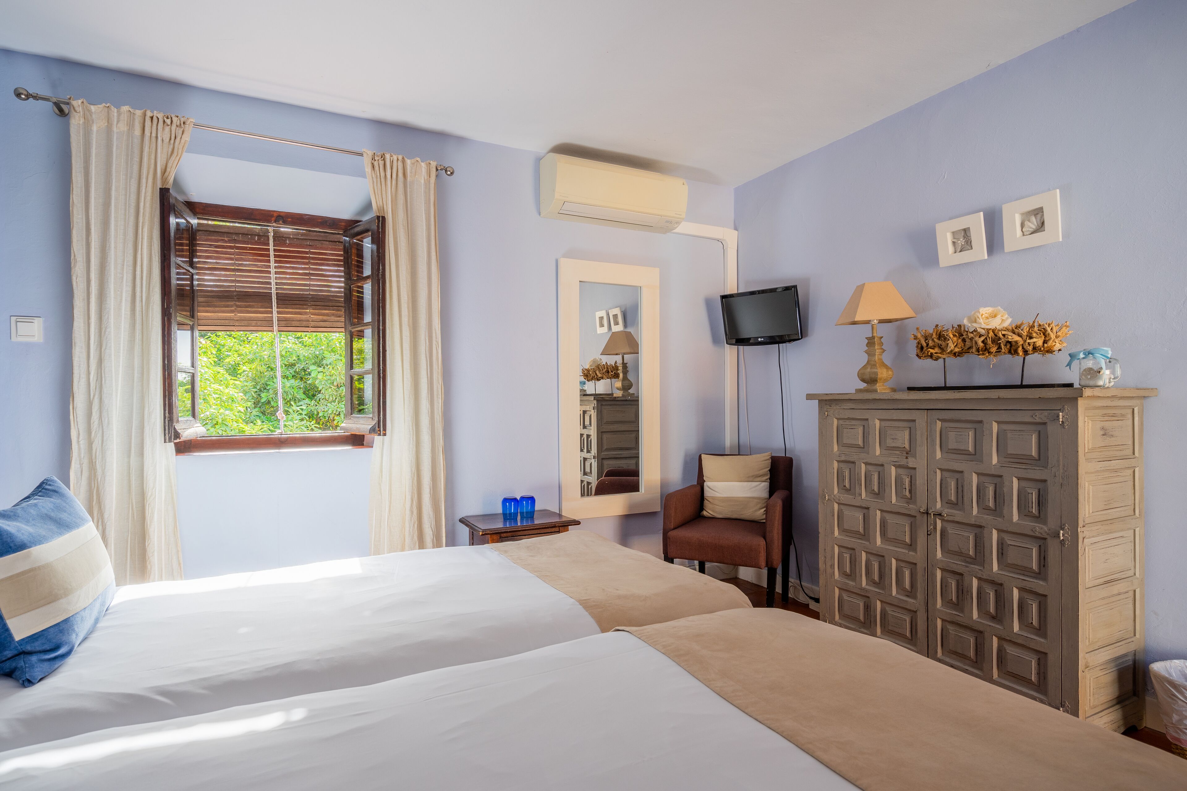 A hotel room with two beds, a TV, a mirror, a dresser, and a window with curtains.