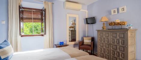 A hotel room with two beds, a TV, a mirror, a dresser, and a window with curtains.