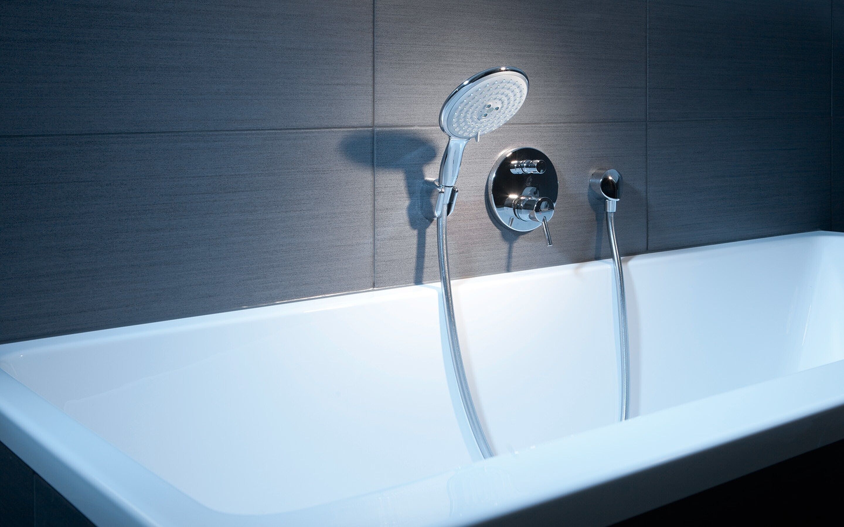 Une salle de bain moderne avec une baignoire blanche, une douchette à main et un panneau de commande fixé au mur.