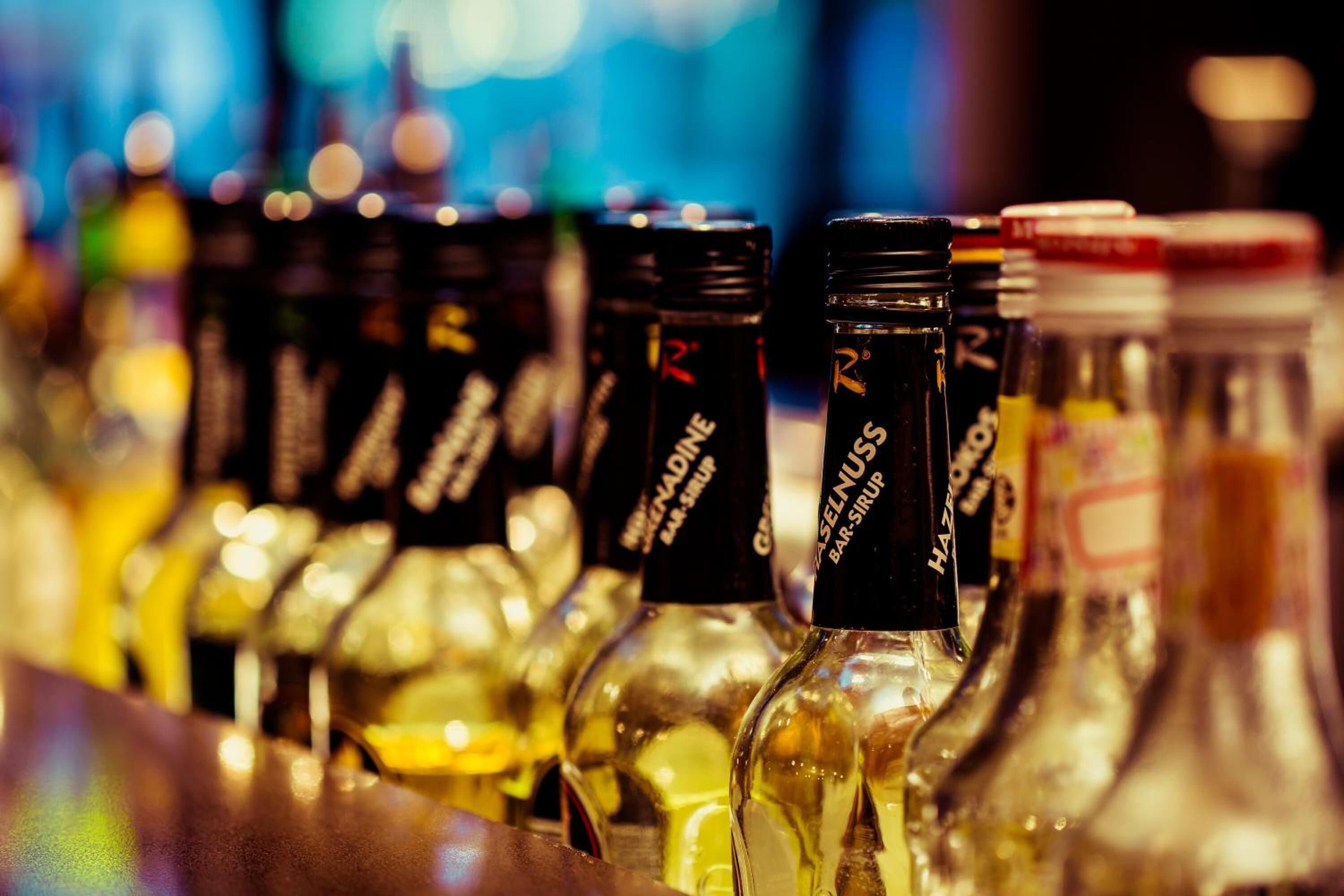 A row of bottles with labels, likely containing beverages, arranged on a bar counter.