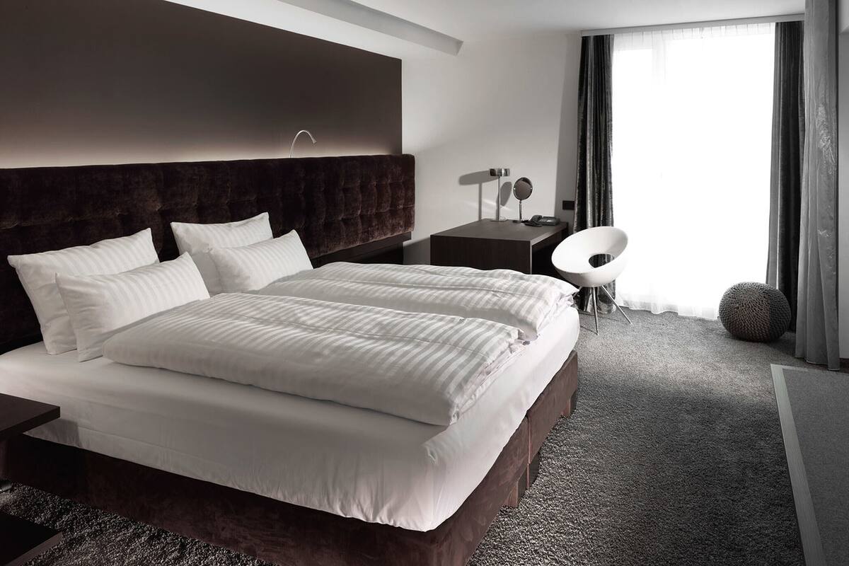 Habitación de hotel moderna con una cama grande, un escritorio, una silla y vistas al exterior.