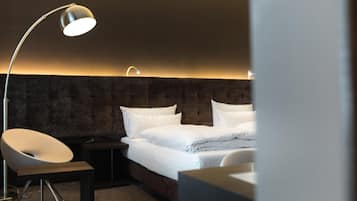 A modern hotel room with a bed, a desk, a chair, and a floor lamp.