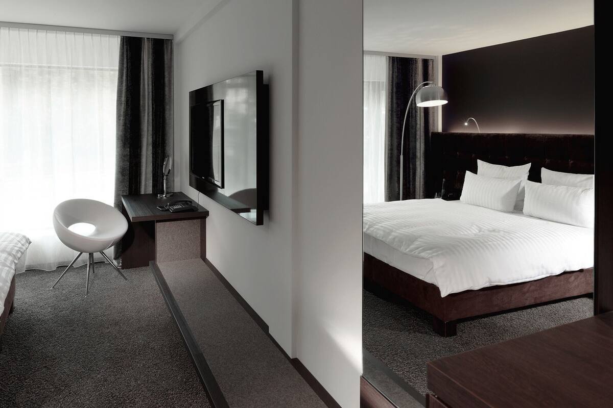 Habitación de hotel con cama, escritorio, silla, televisor y un espejo grande.