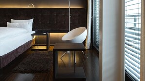 Een moderne slaapkamer met een bed, een stoel, een vloerlamp en een groot raam met jaloezieën.